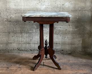 This lot features an antique Eastlake Victorian carved walnut parlor table with a marble top that measures, 28.5” H x 24” W x 16” D.
