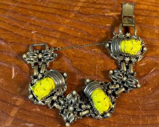 This lot features an unmarked "Asian Princess" bracelet in the style of Selro Selini. This bracelet features yellow molded plastic faces set in ornate, dark metal links. Measures 5-6” depending on use of safety chain. 
