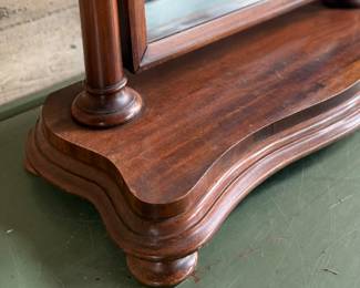 This lot features an antique American Empire gentleman’s shaving mirror with a tilt-top frame, fluted upright supports, and a shaped base with bun feet. This mirror measures, 33” H x 30” W x 12” D.
