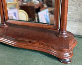 This lot features an antique American Empire gentleman’s shaving mirror with a tilt-top frame, fluted upright supports, and a shaped base with bun feet. This mirror measures, 33” H x 30” W x 12” D.
