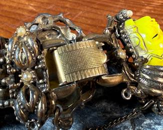 This lot features an unmarked "Asian Princess" bracelet in the style of Selro Selini. This bracelet features yellow molded plastic faces set in ornate, dark metal links. Measures 5-6” depending on use of safety chain. 
