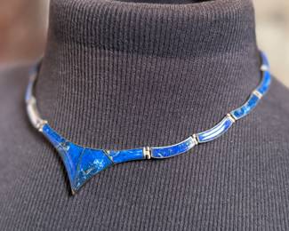 This lot features a vintage silver lapis modernist set including a hinged bib necklace, a bracelet, and earrings. Marked .970 silver with a total approx. weight of 51.89 grams. The necklace measures 16”, bracelet 8”, and earrings 1.5” H.

