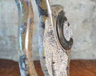 This lot features a stunning polished fossil sculpture featuring embedded ammonite and orthoceras fossils. This sculpture measures, 17.5” H x 12” W x 4” D.
