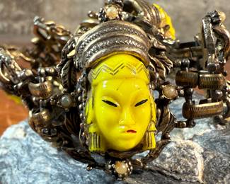 This lot features an unmarked "Asian Princess" bracelet in the style of Selro Selini. This bracelet features yellow molded plastic faces set in ornate, dark metal links. Measures 5-6” depending on use of safety chain. 
