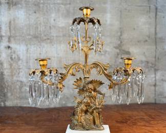 This lot features an antique, mid-19th century Victorian brass triple-light girandole candelabra with crystal prisms and a white marble base. This candelabra measures, 18” H x 15” W x 4” D. 
