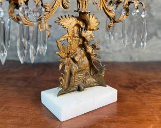 This lot features an antique, mid-19th century Victorian brass triple-light girandole candelabra with crystal prisms and a white marble base. This candelabra measures, 18” H x 15” W x 4” D. 
