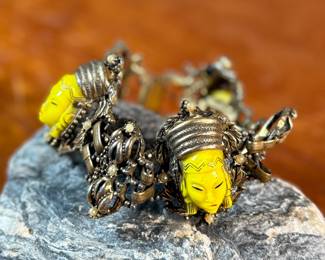 This lot features an unmarked "Asian Princess" bracelet in the style of Selro Selini. This bracelet features yellow molded plastic faces set in ornate, dark metal links. Measures 5-6” depending on use of safety chain. 
