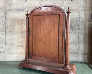 This lot features an antique American Empire gentleman’s shaving mirror with a tilt-top frame, fluted upright supports, and a shaped base with bun feet. This mirror measures, 33” H x 30” W x 12” D.
