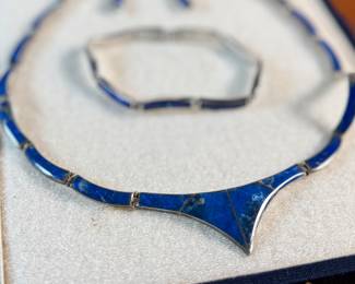 This lot features a vintage silver lapis modernist set including a hinged bib necklace, a bracelet, and earrings. Marked .970 silver with a total approx. weight of 51.89 grams. The necklace measures 16”, bracelet 8”, and earrings 1.5” H.
