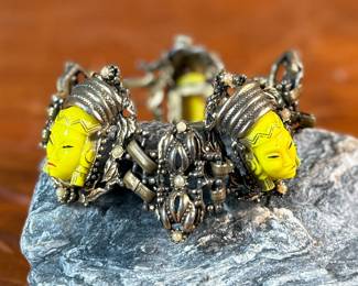 This lot features an unmarked "Asian Princess" bracelet in the style of Selro Selini. This bracelet features yellow molded plastic faces set in ornate, dark metal links. Measures 5-6” depending on use of safety chain. 
