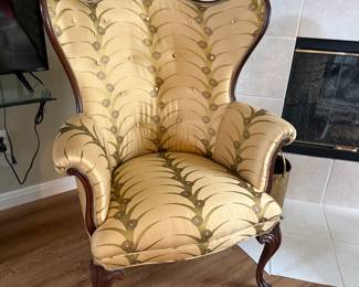 Queen Anne style wingback accent chair with a carved wood frame and cabriole legs, upholstered in a gold and green patterned fabric. 