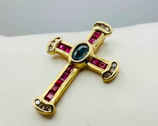 1" gold cross pendant stamped "14K" set with rubies and diamonds with an oval cut sapphire at the center. 2.52 gtw. 