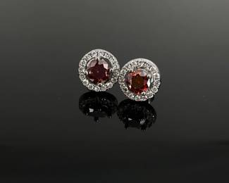 Sparkling red 1 ct watermelon moissanites sit at the center of each earring, surrounded by a halo of clear stones, possibly cubic zirconias. Set in unmarked silver tone. GRA certificate of authenticity included.