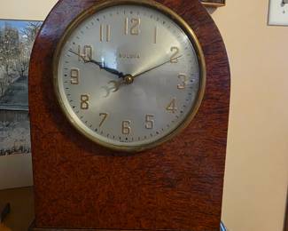 vintage Bulova mantel clock, likely a model from the mid-20th century, featuring a wood case with a burl wood veneer finish and an arched top. 