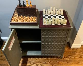 A stylish accent cabinet with decorative circle and teardrop doors provides practical storage.  2 complete chess sets. One set, crafted from stones, exhibits some wear and tear and chips. The other set, contained in a box, is missing the board.