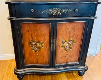 This is a vintage, distressed black finish sideboard or dining room chest with a curved drawer front and hand-painted floral motifs on the drawer and bowed doors.