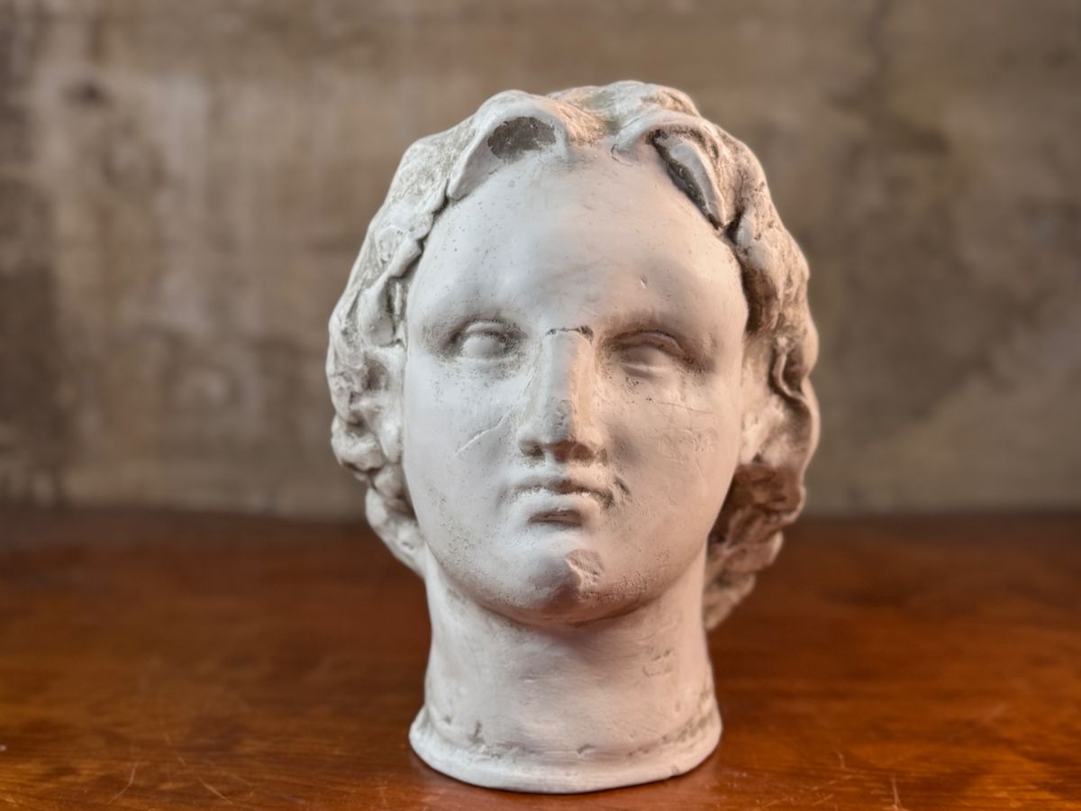 This lot features a head of a statue of Alexander the Great. Appears to be made of a heavy plaster and measures, 10.5” H x 8” W x 9” D.
