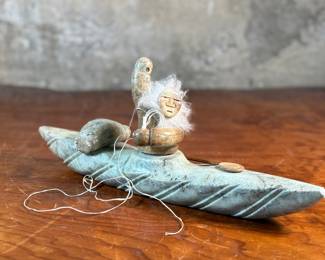 This lot features a hand-carved soapstone sculpture of an Inuit hunter and kayak. Signed underneath and measures, 6” H x 15” W x 3” D. The hunter has come detached as shown in photos and can sit just fine or be reattached.
