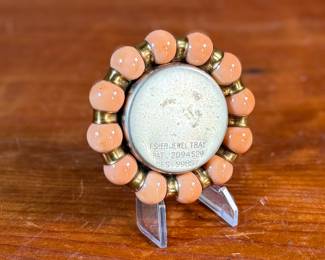 This lot features a Fisher Jewel Tray commemorating the 1939 New York World’s Fair. The tray is made of hammered brass with a ring of coral-colored vitro agate marbles around the outer circumference. These small trays were originally designed to hold ladies’ jewelry. 
