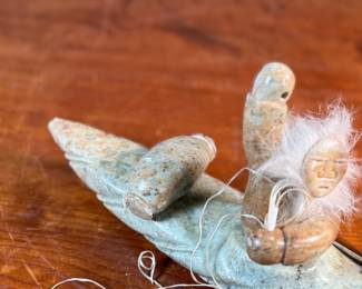 This lot features a hand-carved soapstone sculpture of an Inuit hunter and kayak. Signed underneath and measures, 6” H x 15” W x 3” D. The hunter has come detached as shown in photos and can sit just fine or be reattached.
