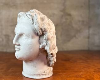 This lot features a head of a statue of Alexander the Great. Appears to be made of a heavy plaster and measures, 10.5” H x 8” W x 9” D.
