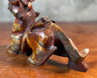 This lot features a beautiful ochre, copper, and viridescent example of a Chinese Pixiu. The creature is depicted with mouth agape, and standing in a fighting stance, his tail twitches behind him frozen in time. Pixiu is a Chinese mythical hybrid creature. Pixiu are considered powerful protectors of the souls of the dead, and resemble strong, winged lions. This sculpture of a Pixiu measures, 7” H x 3” W x 9” D.
