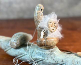 This lot features a hand-carved soapstone sculpture of an Inuit hunter and kayak. Signed underneath and measures, 6” H x 15” W x 3” D. The hunter has come detached as shown in photos and can sit just fine or be reattached.
