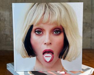 This lot features a 2022 “calendar” by Bryan Adams for Pirelli titled, “On the Road”. A unique book full of famous photographs. A collectible edition in the original slipcase. Bryan Adams is known for photographing the 2022 Pirelli Calendar, which is titled “On the Road” and features portraits of various musicians like Cher, Iggy Pop, Jennifer Hudson, and Rita Ora. Adams, a successful photographer as well as a musician, created the calendar to capture the glamour and loneliness of a musician’s life on tour.
