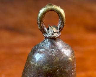 This lot features an antique African brass cattle bell that measures, 7” H x 4” W x 4” D.
