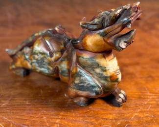 This lot features a beautiful ochre, copper, and viridescent example of a Chinese Pixiu. The creature is depicted with mouth agape, and standing in a fighting stance, his tail twitches behind him frozen in time. Pixiu is a Chinese mythical hybrid creature. Pixiu are considered powerful protectors of the souls of the dead, and resemble strong, winged lions. This sculpture of a Pixiu measures, 7” H x 3” W x 9” D.
