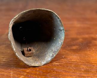 This lot features an antique African brass cattle bell that measures, 7” H x 4” W x 4” D.
