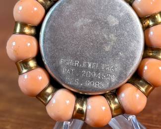 This lot features a Fisher Jewel Tray commemorating the 1939 New York World’s Fair. The tray is made of hammered brass with a ring of coral-colored vitro agate marbles around the outer circumference. These small trays were originally designed to hold ladies’ jewelry. 
