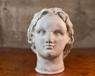 This lot features a head of a statue of Alexander the Great. Appears to be made of a heavy plaster and measures, 10.5” H x 8” W x 9” D.