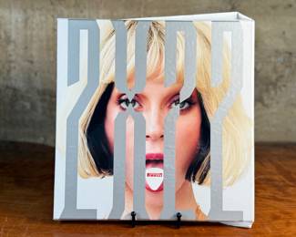 This lot features a 2022 “calendar” by Bryan Adams for Pirelli titled, “On the Road”. A unique book full of famous photographs. A collectible edition in the original slipcase. Bryan Adams is known for photographing the 2022 Pirelli Calendar, which is titled “On the Road” and features portraits of various musicians like Cher, Iggy Pop, Jennifer Hudson, and Rita Ora. Adams, a successful photographer as well as a musician, created the calendar to capture the glamour and loneliness of a musician’s life on tour.
