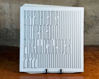 This lot features a 2022 “calendar” by Bryan Adams for Pirelli titled, “On the Road”. A unique book full of famous photographs. A collectible edition in the original slipcase. Bryan Adams is known for photographing the 2022 Pirelli Calendar, which is titled “On the Road” and features portraits of various musicians like Cher, Iggy Pop, Jennifer Hudson, and Rita Ora. Adams, a successful photographer as well as a musician, created the calendar to capture the glamour and loneliness of a musician’s life on tour.
