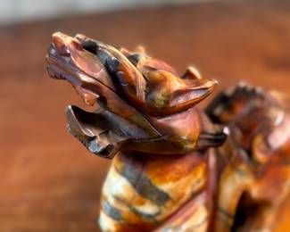 This lot features a beautiful ochre, copper, and viridescent example of a Chinese Pixiu. The creature is depicted with mouth agape, and standing in a fighting stance, his tail twitches behind him frozen in time. Pixiu is a Chinese mythical hybrid creature. Pixiu are considered powerful protectors of the souls of the dead, and resemble strong, winged lions. This sculpture of a Pixiu measures, 7” H x 3” W x 9” D.
