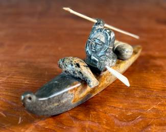 "Hunter and Kayak", an Inuit hand-carved sculpture, likely made of soapstone by listed artist, Arnold Kayutak. Signed underneath as shown in photos and measures, 4” H x 9.5” W x 4” D.
