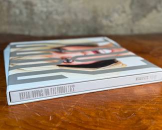 This lot features a 2022 “calendar” by Bryan Adams for Pirelli titled, “On the Road”. A unique book full of famous photographs. A collectible edition in the original slipcase. Bryan Adams is known for photographing the 2022 Pirelli Calendar, which is titled “On the Road” and features portraits of various musicians like Cher, Iggy Pop, Jennifer Hudson, and Rita Ora. Adams, a successful photographer as well as a musician, created the calendar to capture the glamour and loneliness of a musician’s life on tour.
