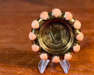 This lot features a Fisher Jewel Tray commemorating the 1939 New York World’s Fair. The tray is made of hammered brass with a ring of coral-colored vitro agate marbles around the outer circumference. These small trays were originally designed to hold ladies’ jewelry. 
