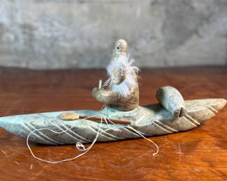 This lot features a hand-carved soapstone sculpture of an Inuit hunter and kayak. Signed underneath and measures, 6” H x 15” W x 3” D. The hunter has come detached as shown in photos and can sit just fine or be reattached.
