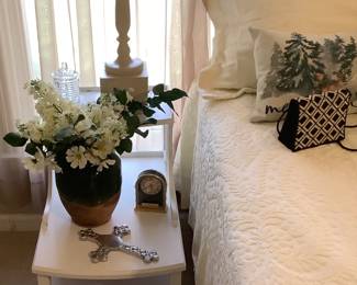 White end table by King Size bed with remote control. Bed frame by Reverie and has a remote control.