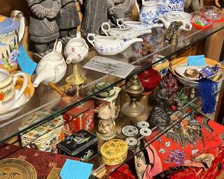 Eclectic glass-case display of antique and vintage Asian-inspired décor and collectibles. Includes blue-and-white porcelain, teapots, figurines, carved stone and metal sculptures, incense burners, boxes, and assorted small decorative objects. Rich mix of materials, textures, and cultural motifs with visible age and patina. Ideal for collectors and decorative display. All items sold as-is.