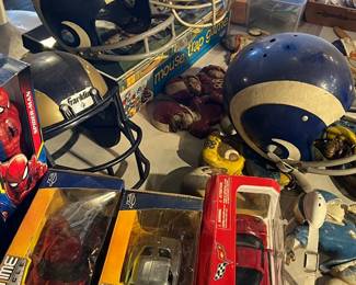 Collection of vintage and novelty sports memorabilia featuring old football helmets, figurines, and boxed model cars. Includes early-style helmets with heavy wear and patina, paired with modern collectible toys and display pieces. A fun mix for sports fans, collectors, or themed décor. All items sold as-is.