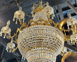 Grand antique crystal chandelier with a monumental tiered form, featuring cascading faceted prisms and ornate gilt metal arms with candle-style lights. A dramatic centerpiece with exceptional scale, sparkle, and old-world elegance. Shows age-appropriate wear and patina. Ideal for grand interiors, restoration, or statement display. All items sold as-is.