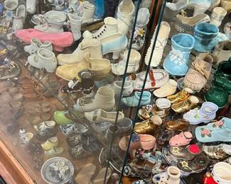 Charming display of miniature porcelain and ceramic collectibles, including small shoes, pitchers, cups, figurines, and novelty vessels in a variety of colors and styles. Arranged densely within a glass display case, offering strong visual appeal and nostalgic charm. Ideal for collectors and decorators. Condition varies; all items sold as-is.
