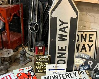 Vintage signage and industrial décor grouping featuring a large “ONE WAY” arrow sign, metal street signs, automotive advertising, and assorted workshop elements. Includes Ford-themed signage, road markers, and metal parts with heavy patina and bold graphic appeal. Ideal for collectors, garages, retail display, or set design. All items sold as-is.