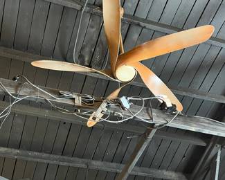 Vintage industrial ceiling fan featuring wide wooden blades and a central metal housing, suspended from the ceiling with original mounting hardware. Striking mid-century or early industrial design with visible age and patina. Ideal for restoration, loft-style interiors, or decorative display. Functionality untested. All items sold as-is.
