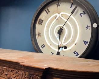 Vintage neon wall clock featuring an illuminated circular neon tube set behind a classic clock face with numerals and star accents. Housed in a metal case and suspended by chain, offering strong mid-century character and visual appeal. Condition reflects age; neon and clock functionality untested. Ideal for collectors, bars, or statement décor. All items sold as-is.