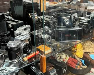 Extensive collection of vintage cameras and photographic equipment displayed in a glass case. Includes a wide variety of film cameras, lenses, accessories, and related gear from multiple eras and makers. Strong appeal for collectors, photographers, and display. Condition varies; functionality untested. All items sold as-is.