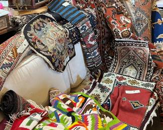 Richly layered assortment of vintage and antique textiles, including decorative pillows, cushions, and folded rugs with intricate woven patterns and bold colors. Features tribal, Persian-style, and folk-inspired designs creating a warm, collected look. Ideal for decorators, collectors, or interior styling. Condition varies; all items sold as-is.